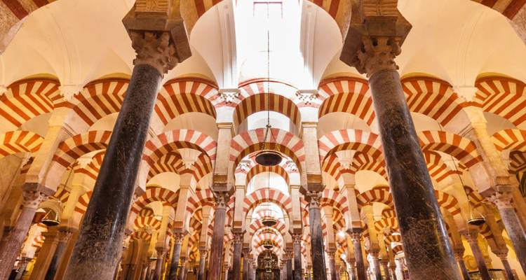 Wide interior view of Cordoba’s Mezquita with repeating striped arches and soaring columns illuminated by skylight.