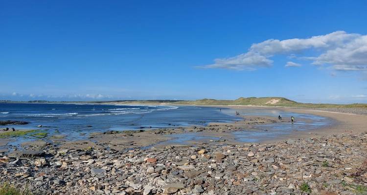 Baie sablonneuse et spacieuse avec des vagues douces, rivage rocheux et ciel bleu clair par une journée ensoleillée