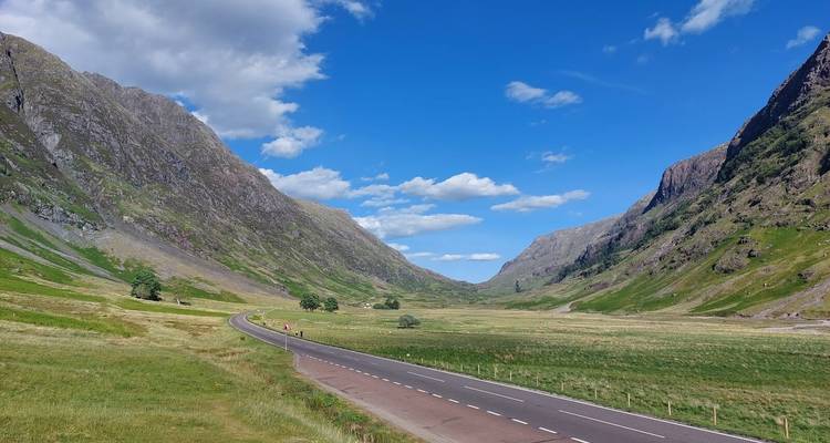 Vallée des Highlands ouverte avec une route sinueuse flanquée de montagnes vertes escarpées sous un ciel bleu éclatant