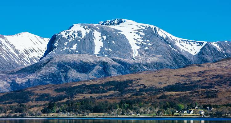 Snow-capped Ben Nevis rising above brown moorland reflected in a still loch