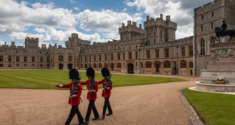 Königliche Gardisten in roten Uniformjacken marschieren über den Innenhof von Schloss Windsor unter teilweise bewölktem Himmel