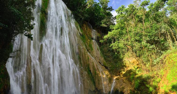 Tall tropical waterfall cascading down moss-covered cliffs surrounded by lush green forest.