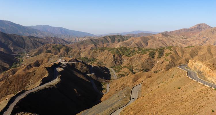 Vue panoramique des routes de montagne sinueuses traversant les crêtes accidentées du Haut Atlas sous un ciel bleu dégagé