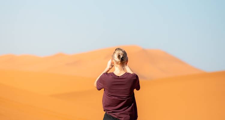 Vue arrière d'un voyageur photographiant des dunes de sable orange vif sur un ciel bleu