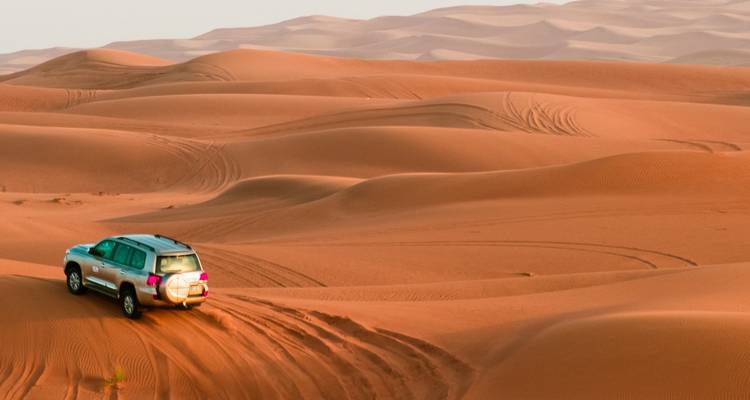 Un SUV circulant sur des dunes ondulées en laissant des traces profondes à travers une mer de sable