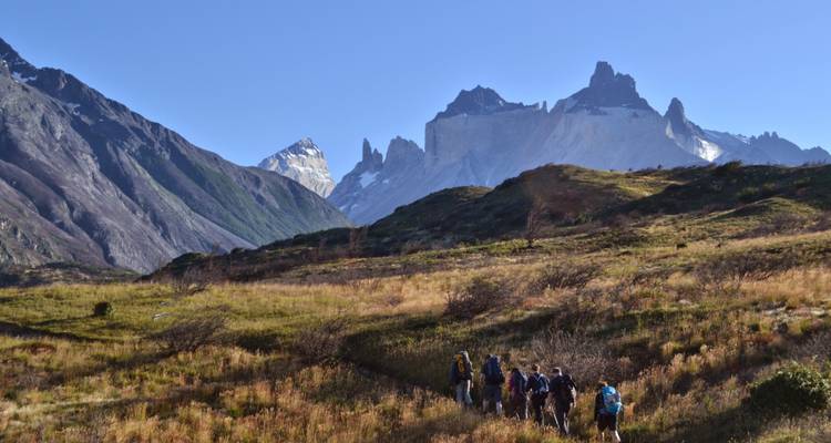 Eine Trekking-Gruppe wandert durch offene patagonische Ebenen auf die dramatischen Felsspitzen der Torres del Paine unter klarem Himmel zu.