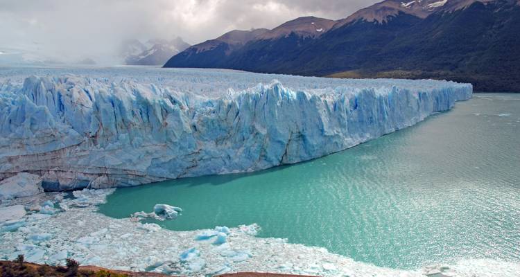 Die gigantische blaue Wand des Perito-Moreno-Gletschers erhebt sich über türkisfarbenem Wasser, das von Eisbergen geprägt ist.