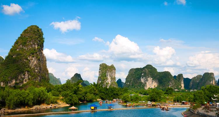 Karst limestone peaks and blue river with bamboo rafts in Yangshuo countryside under bright sky.
