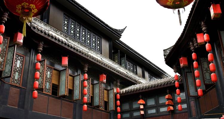 Traditional Chinese courtyard buildings with ornate wooden windows are strung with bright red lanterns against a white sky.