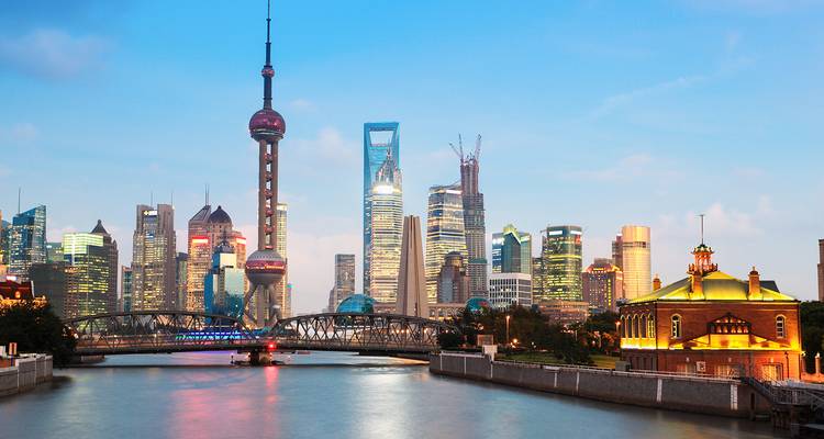 Ikonische Skyline von Shanghai mit dem Oriental Pearl Tower und modernen Wolkenkratzern, die sich bei Einbruch der Dunkelheit über dem Huangpu-Fluss erheben