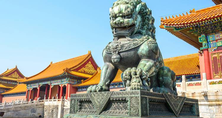 Bronzene Wächterlöwenstatue, die die großen rot-goldenen Tore der Verbotenen Stadt Pekings unter einem klaren blauen Himmel bewacht
