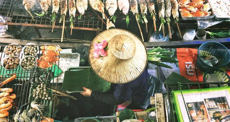 Bovenaanzicht van een verkoper die zeevruchten grilt op een drukke Thaise drijvende markt.