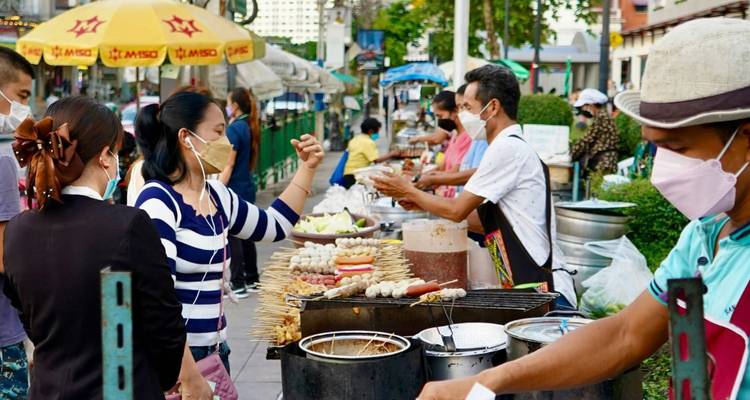 Mercado de comida al aire libre lleno de gente donde vendedores con mascarilla preparan pinchos y snacks para los clientes hambrientos.