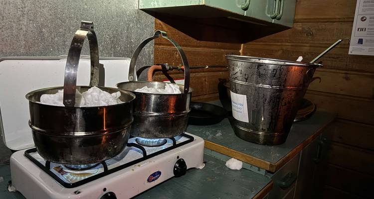 Metal pots filled with snow melt on gas burners inside a rustic wooden hut.