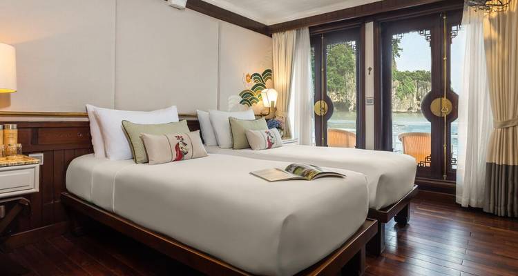 Elegante camarote doble con grandes ventanas con vistas a los picos de piedra caliza de la Bahía de Halong, amueblado en tonos de madera cálida.
