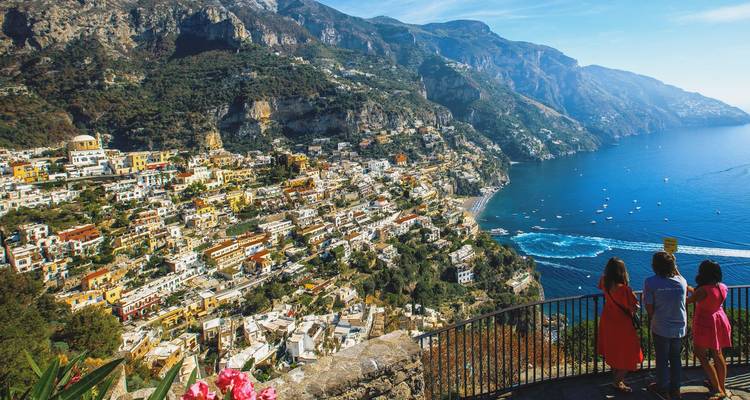 Vista panorámica del colorido Positano cayendo en cascada por los acantilados con tres turistas admirando la Costa de Amalfi.
