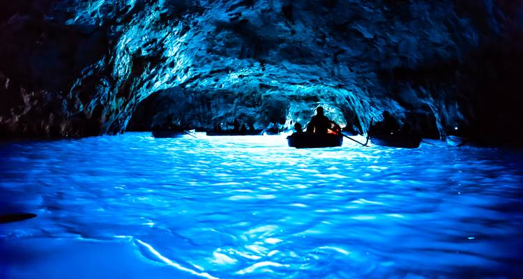 Barcas recortadas contra el cielo dentro de la luminosa Gruta Azul de Capri donde el agua brilla de un azul eléctrico.