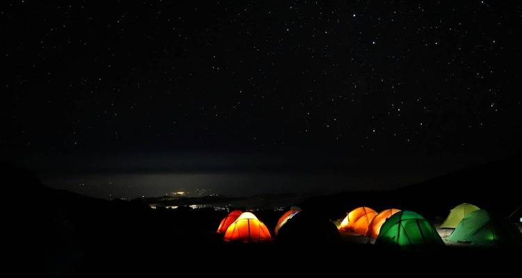 Nachtscène van gloeiende tenten onder een sterrenrijke hemel op de Kilimanjaro, stadslichten ver beneden.