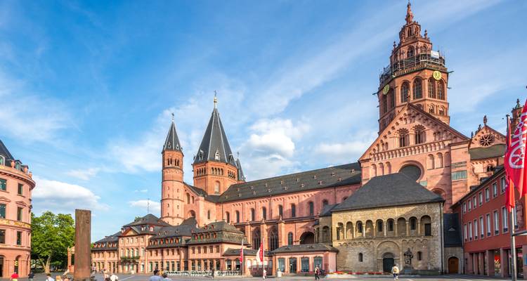 De sierlijke rode zandsteen Mainzer Dom domineert een zonnig plein onder een blauwe hemel met lichte wolken.