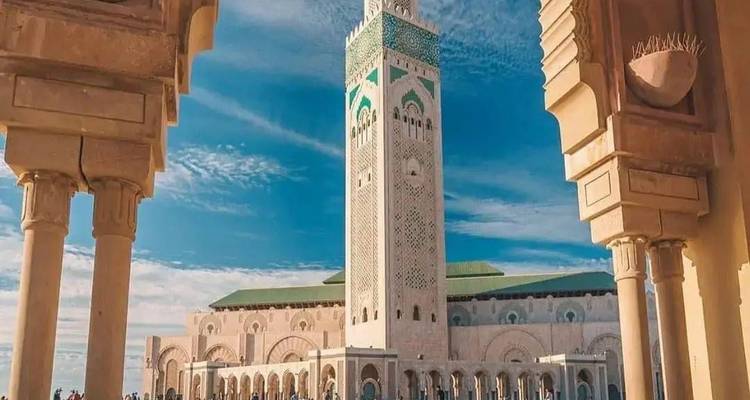 La mosquée Hassan II et son minaret imposant encadrés par des arcs ornementés sur un ciel bleu éclatant.