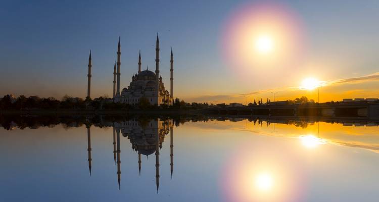 Reflet d'une mosquée aux nombreux minarets et double halo solaire sur un fleuve calme au crépuscule.
