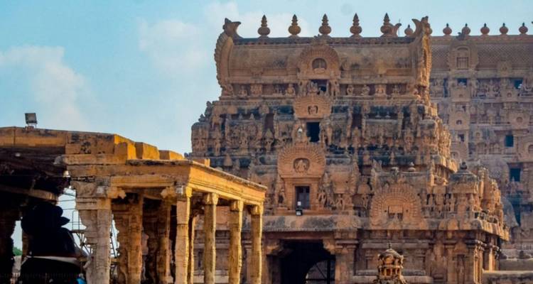 Nahaufnahme von aufwendigen Steinmetzarbeiten und dem aufragenden Gopuram des Brihadeeswarar-Tempels unter blauem Himmel
