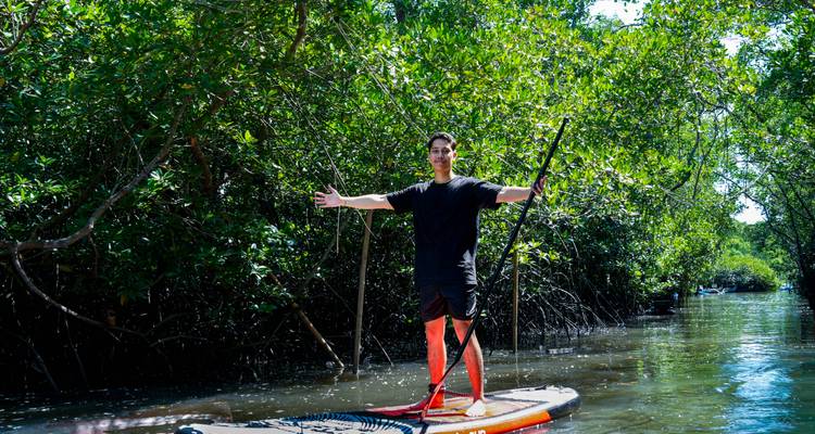 Pagayeur souriant s'étirant les bras grand ouvert dans un chenal de mangrove parsemé de lumière solaire