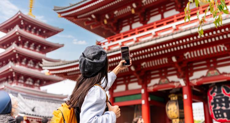 Traveller taking selfie in front of bright red pagoda gate at Senso-ji temple.