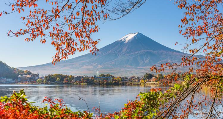 Snow-capped Mount Fuji framed by autumn foliage reflecting on Lake Kawaguchi.