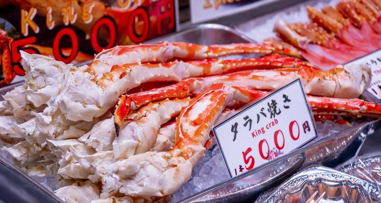 Display of fresh king crab legs on ice at Japanese market with price tags.