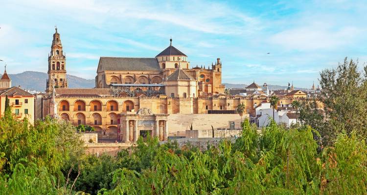 Panoramisch uitzicht op de Mezquita-Kathedraal van Córdoba die uittorent boven weelderig groen en historische ruïnes onder een heldere ochtendhemel.