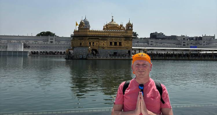 Visitor with hands together in prayer pose before the Golden Temple reflecting in the holy pool