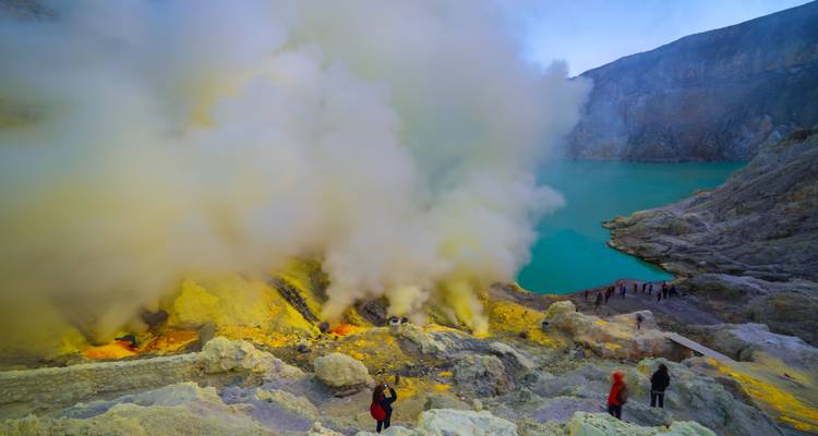 La vapeur de soufre épaisse s'échappe d'une fissure à côté d'un lac d'un bleu éclatant tandis que les visiteurs observent le plancher du cratère.