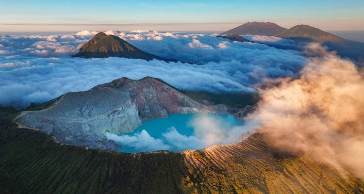 Vue aérienne de la crête du cratère du lac Ijen émergeant au-dessus d'une mer de nuages au lever du soleil.