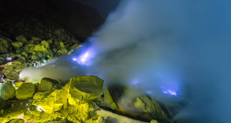 Les évents de soufre nocturnes brillant d'une lueur bleue sous d'épaisses nuages de vapeur, des mineurs visibles parmi les rochers jaunes.
