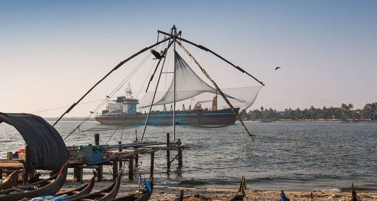 Silhouet van een Chinees visnет en een voorbijvarend vrachtschip op de Arabische Zee bij Kochi in het zonsondergangslicht.