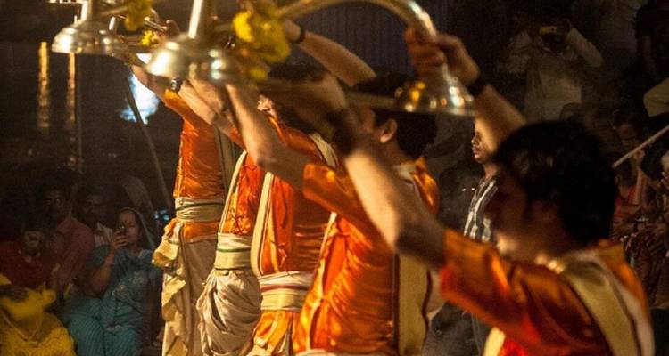 Priests in orange conduct evening ritual with raised lamps before a packed waterfront audience