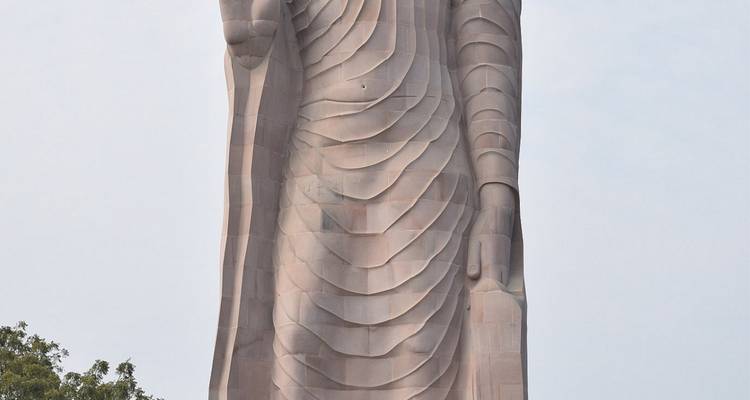 Hohe Sandstein-Buddhastatue, die sich gegen einen blassen Himmel abhebt