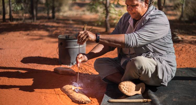 Un guide autochtone démontre la fabrication traditionnelle du feu sur le sable rouge.