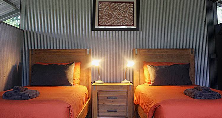 Einfaches Kabineninterieur mit zwei Einzelbetten, bezogen mit orangefarbener Bettwäsche, und warmen Nachttischlampen.