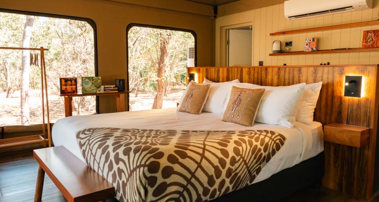Chambre de tente de luxe avec jeté à motifs et vue sur la forêt, similaire à l'intérieur précédent.