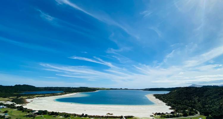 Expansive view of a crescent white-sand beach curving around a tranquil blue bay.