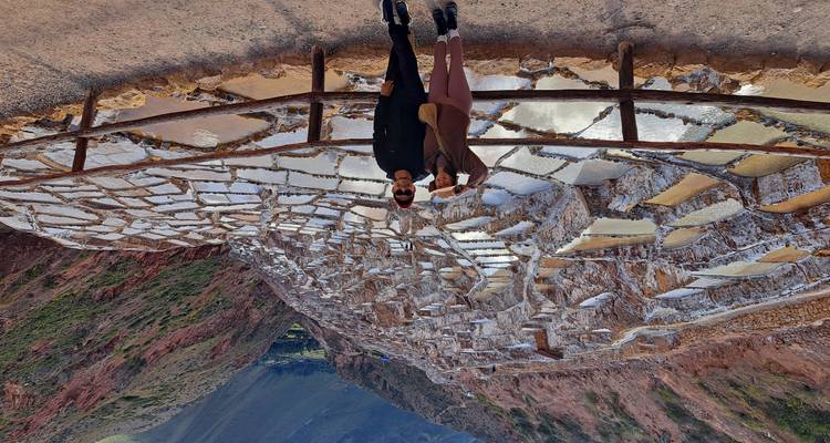 Un couple se tient devant les bassins de sel en escaliers de Maras qui s'étagent dans une vallée accidentée.