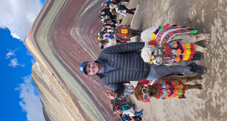 Voyageur souriant avec des alpagas vêtus de couleurs vives devant la Montagne Arc-en-ciel du Pérou.