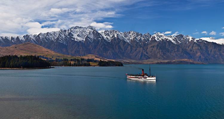 Vintage steamship cruising on Lake Wakatipu with Remarkables mountain range behind.
