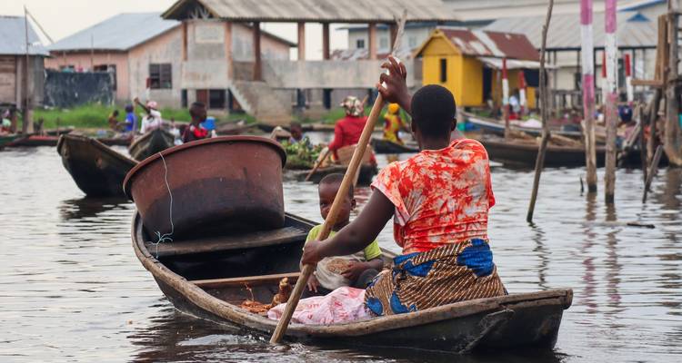 Femme locale naviguant en canoë en bois avec un enfant dans les eaux calmes du village.