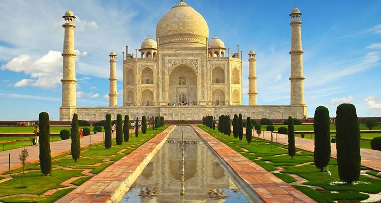 Klassische Ansichtskartenperspektive des Taj Mahal, gespiegelt im langen Spiegelpool unter einem leuchtend blauen Himmel.