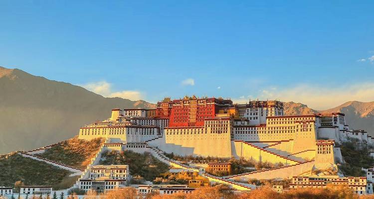 Palacio de Potala iluminado por la cálida luz del atardecer, elevándose sobre Lhasa con montañas de fondo y un cielo despejado.