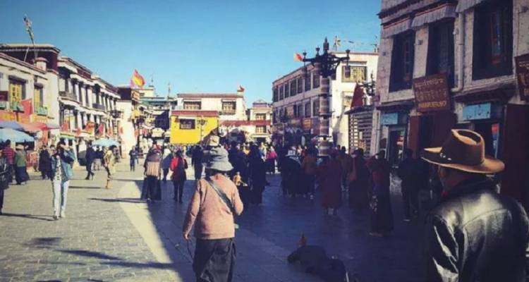 Calle peatonal concurrida repleta de edificios tibetanos y compradores bajo un cielo azul brillante.
