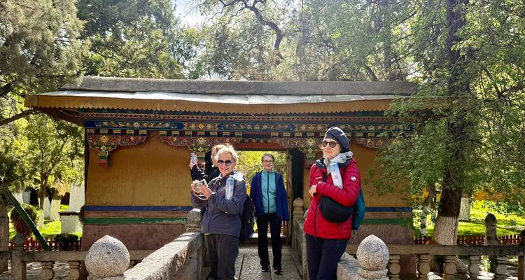Un pequeño grupo de turistas explora una colorida puerta de patio tibetana rodeada de árboles frondosos.